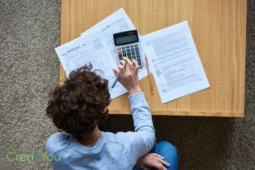 Person rechnet mit Formularen am Tisch, Symbol für Einkommensteuererklärung.