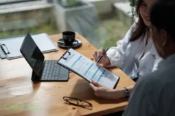 Beratung zur Pflegeversicherung, zwei Personen prüfen Unterlagen auf einem Klemmbrett am Tisch mit Laptop.